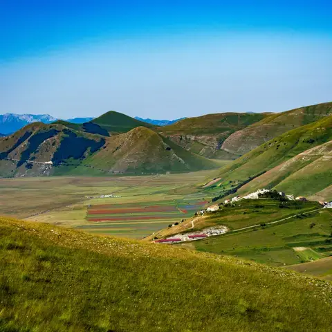 campo di erba verde vicino alla montagna sotto il cielo blu durante il giorno