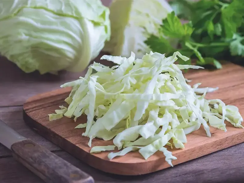 Cavolo cappuccio intero e tagliato sottile su un tagliere iStock