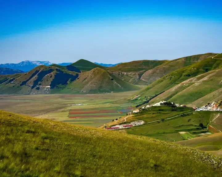 campo di erba verde vicino alla montagna sotto il cielo blu durante il giorno